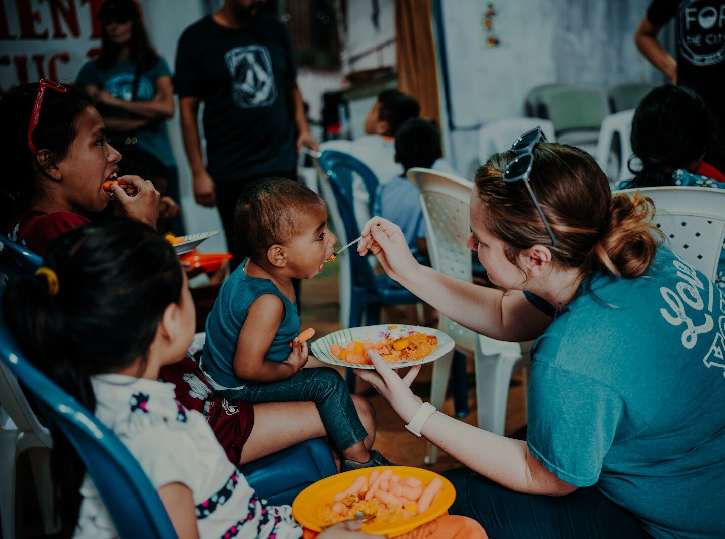 a woman feeding a plate of food to children