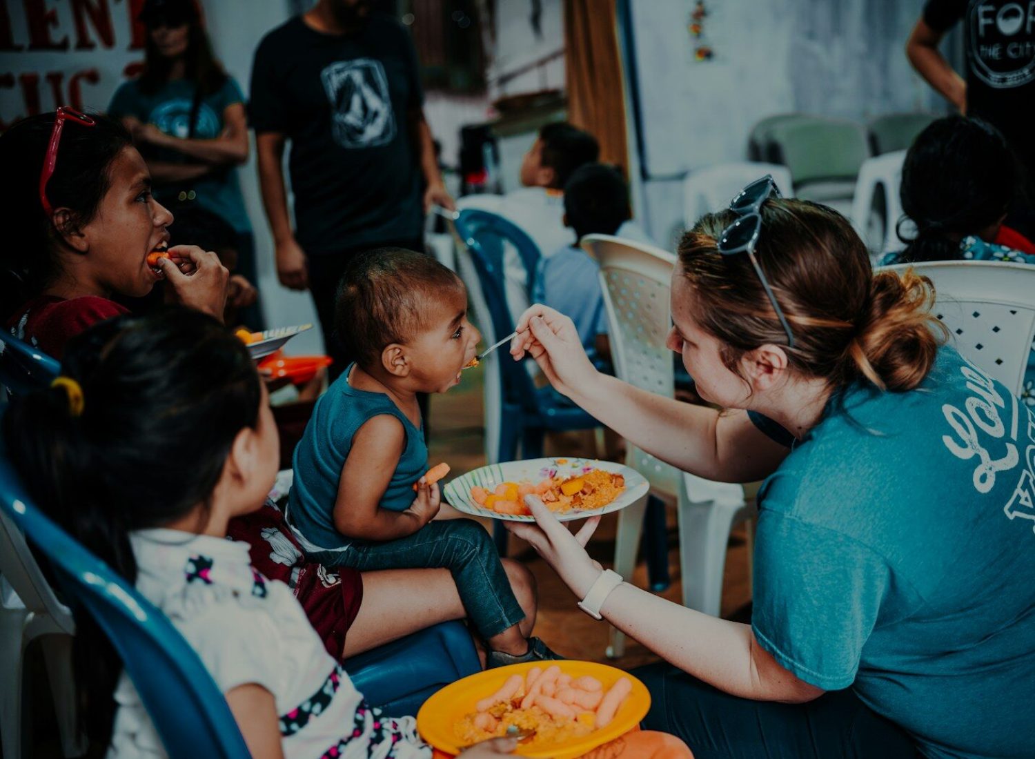 a woman feeding a plate of food to children